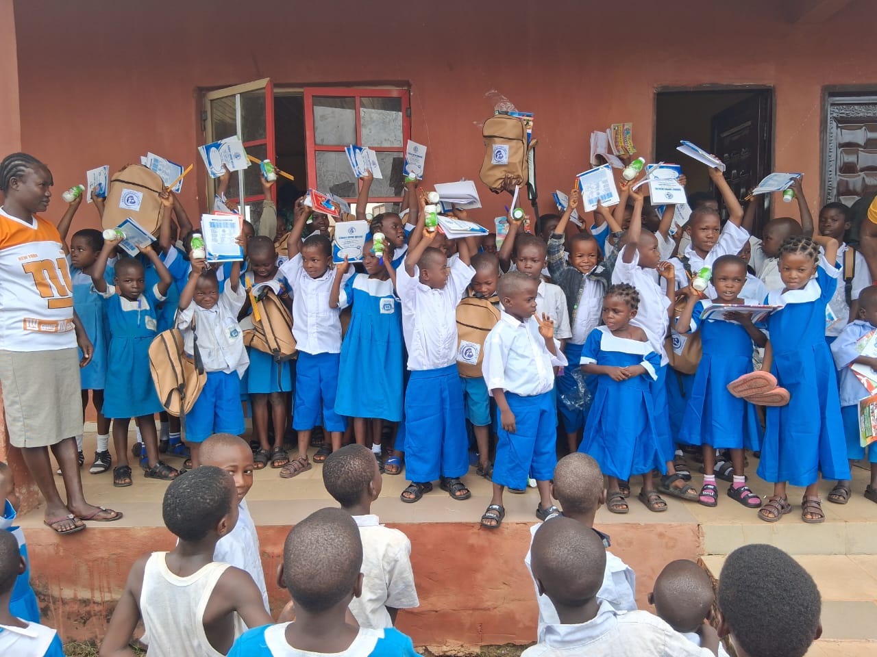 Pupils outside their school raising their new backpacks, books and supplies in celebration