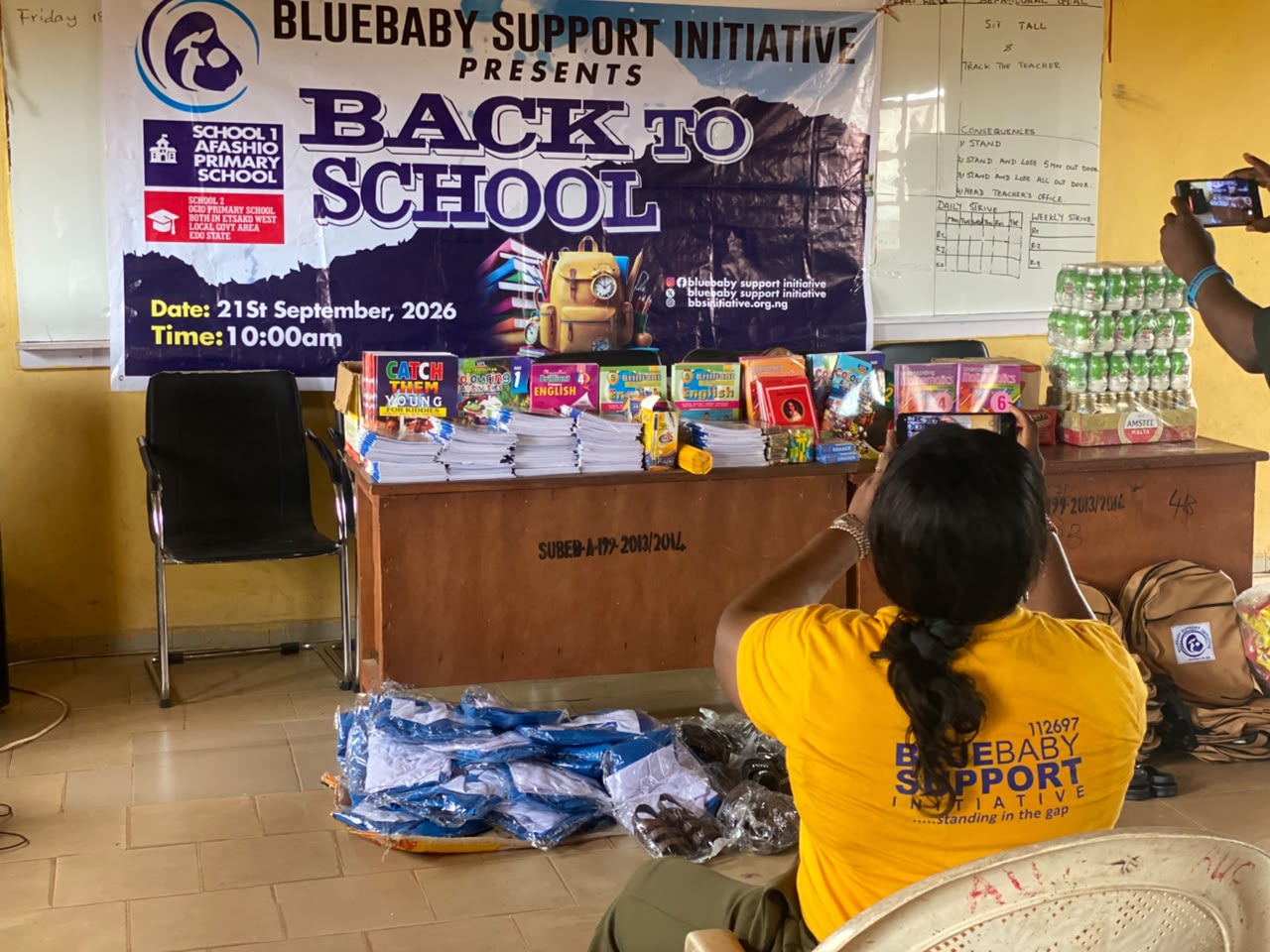 A BBSI volunteer in a yellow BBSI t-shirt photographing the Back to School banner and supplies
