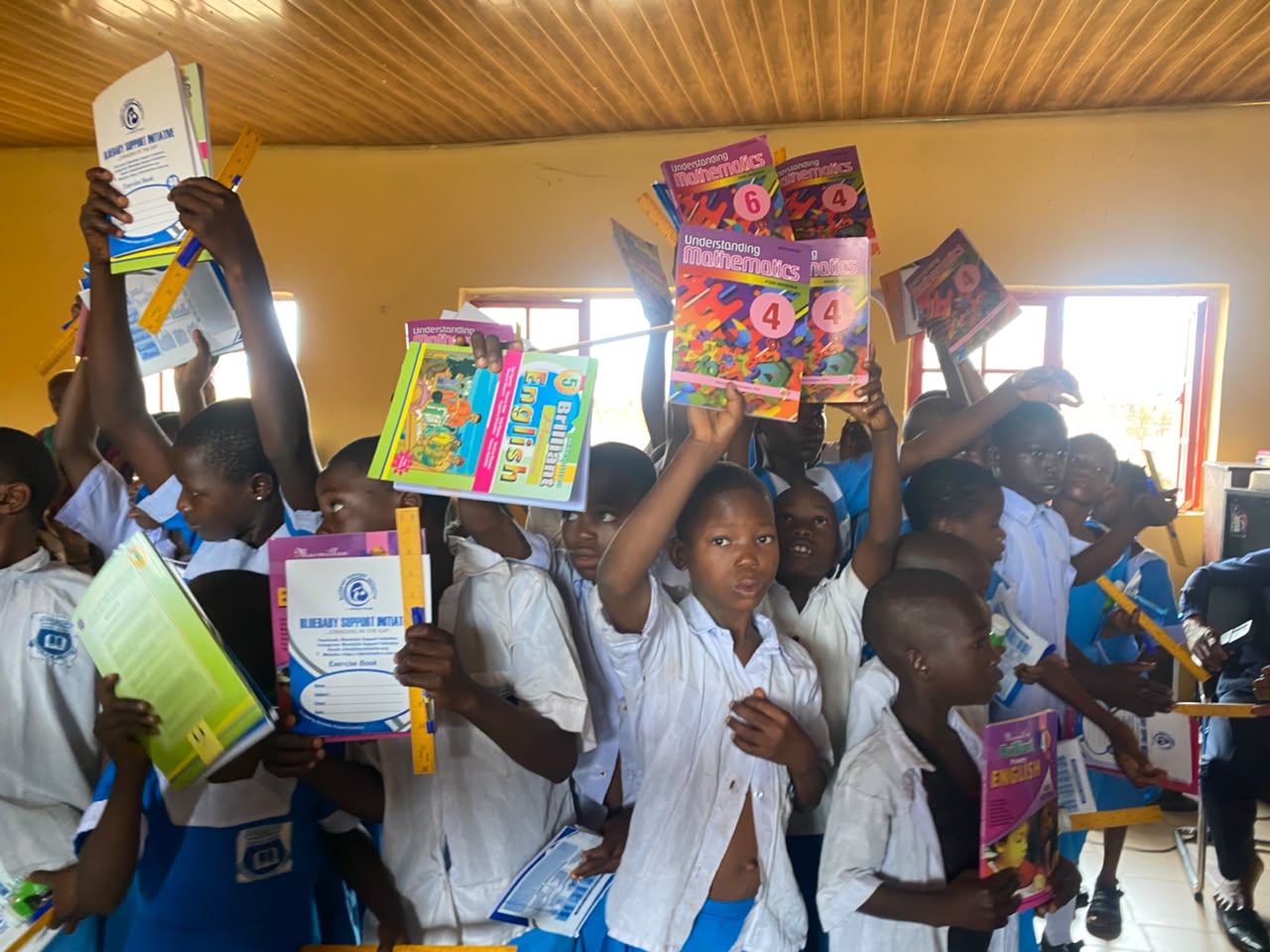 A classroom full of pupils raising their new exercise books, textbooks and rulers