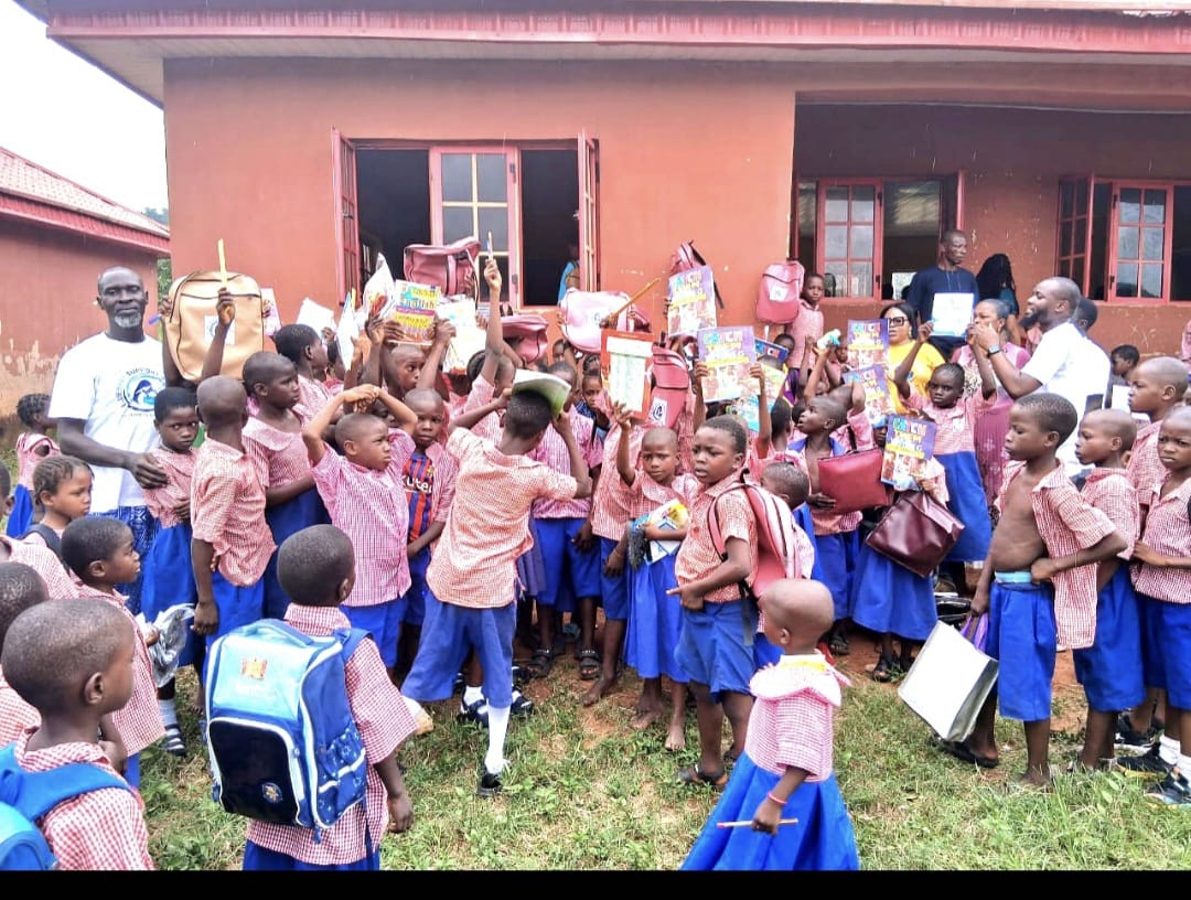 A large group of pupils gathered outside their school holding new backpacks and supplies