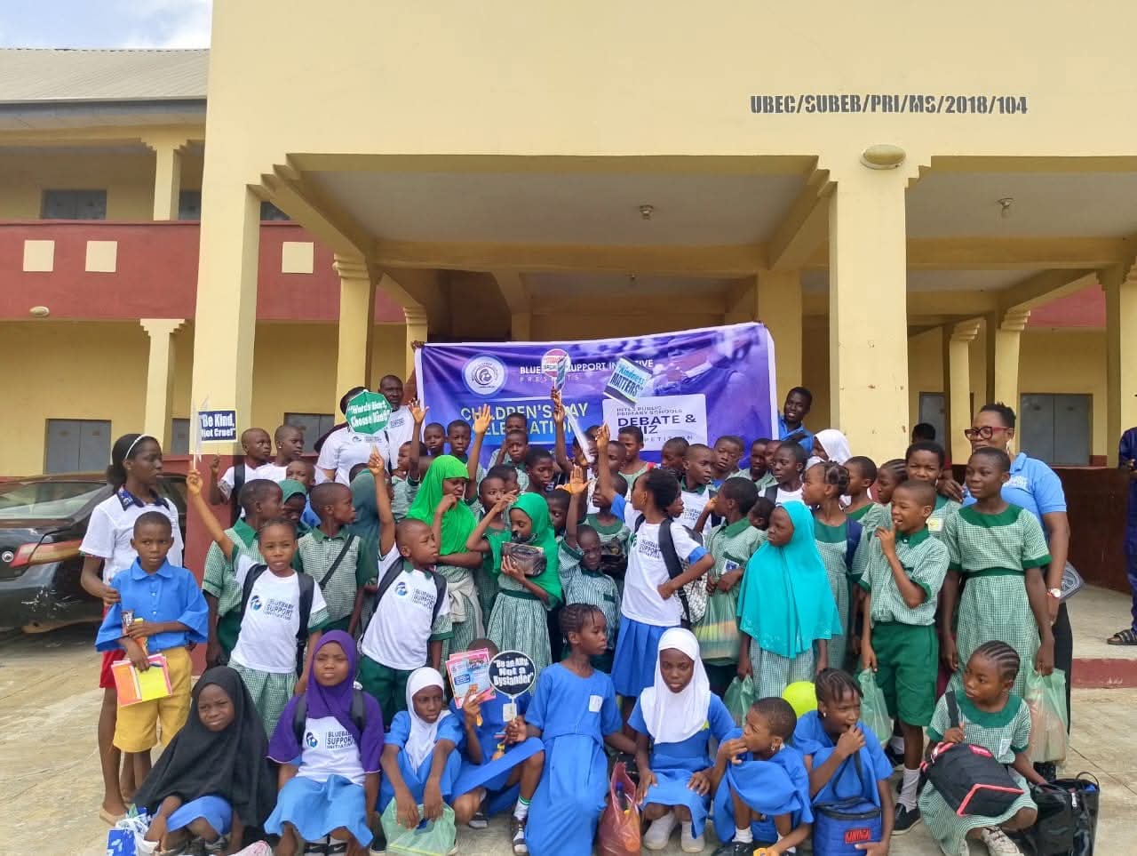 A BBSI volunteer with two children holding their new backpacks in front of a BBSI banner