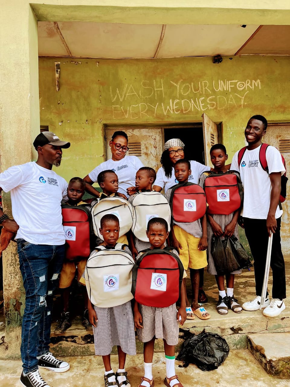 Pupils in a classroom, some in graduation gowns, holding up new backpacks and gift packs